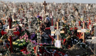 A woman stands by the grave of her relative in the Saint Lazarus cemetery in Chisinau, Moldova, Saturday, Jan. 30, 2016. The Saint Lazarus cemetery is one of the largest in Europe with a surface of  2 million square meters and more than 300 thousand graves and is considered one of the top places to visit in the Moldovan capital. (AP Photo/Vadim Ghirda)